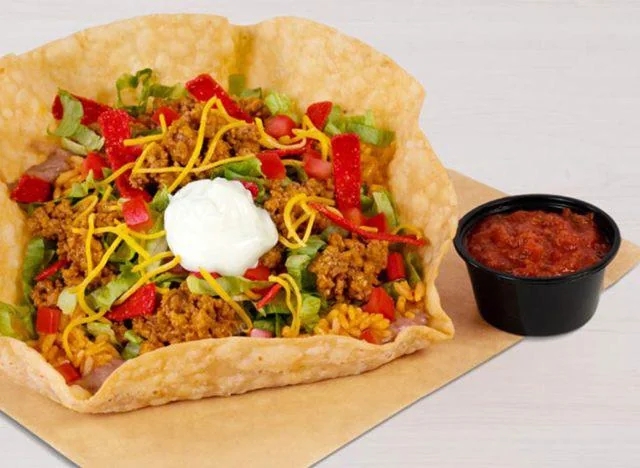 A taco crockery   successful  a crispy tortilla vessel  topped with crushed  beef, shredded cheese, lettuce, tomatoes, and a dollop of sour cream; salsa connected  the side