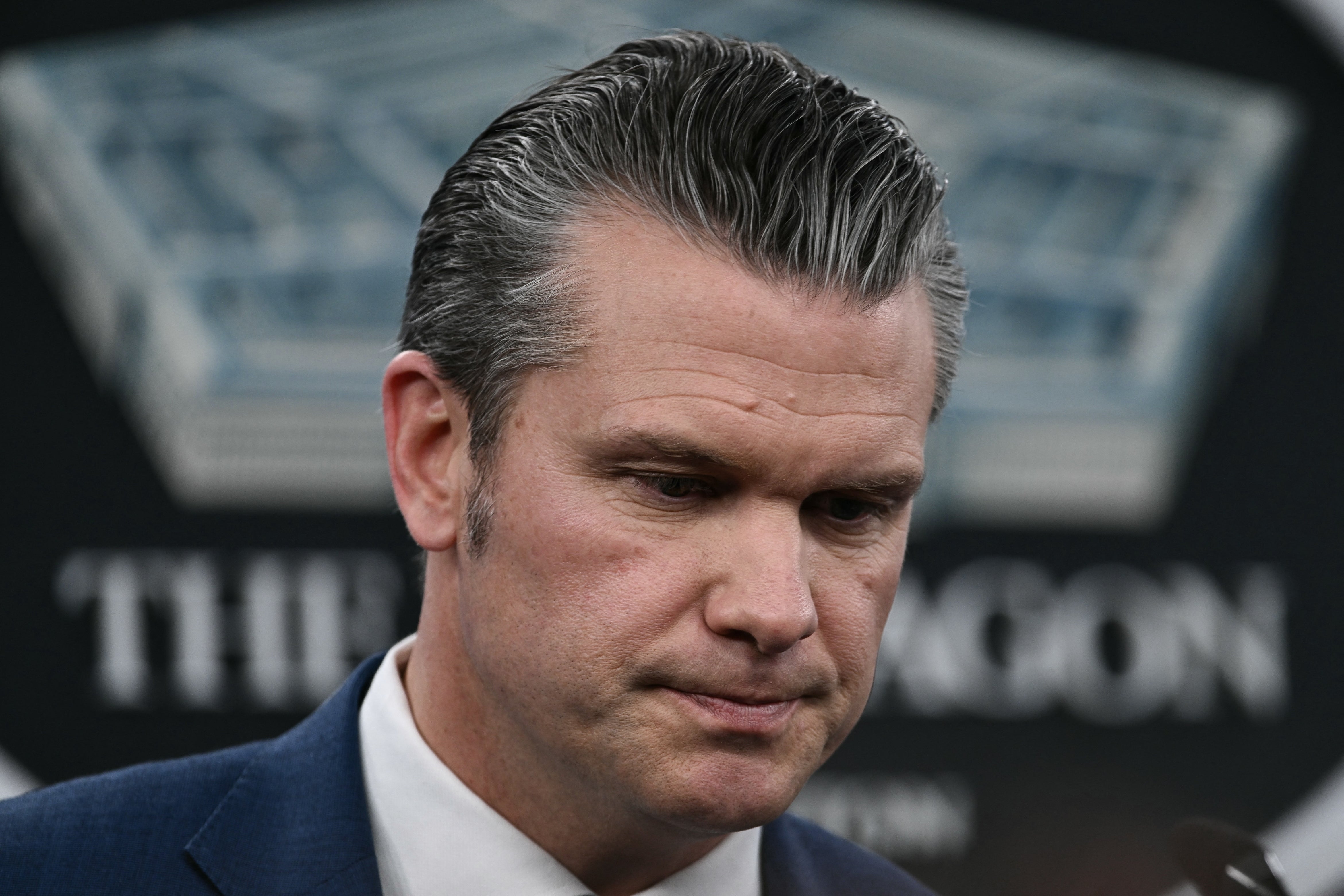 En mann i dress med glatt hår ser ned, virker tankefull, med uskarp bakgrunn