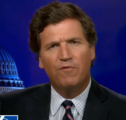 Man in a suit and tie speaks against a backdrop with a dome building, possibly a TV show or news broadcast setting