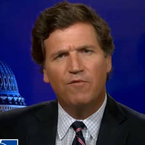 Man in a suit and tie speaks against a backdrop with a dome building, possibly a TV show or news broadcast setting