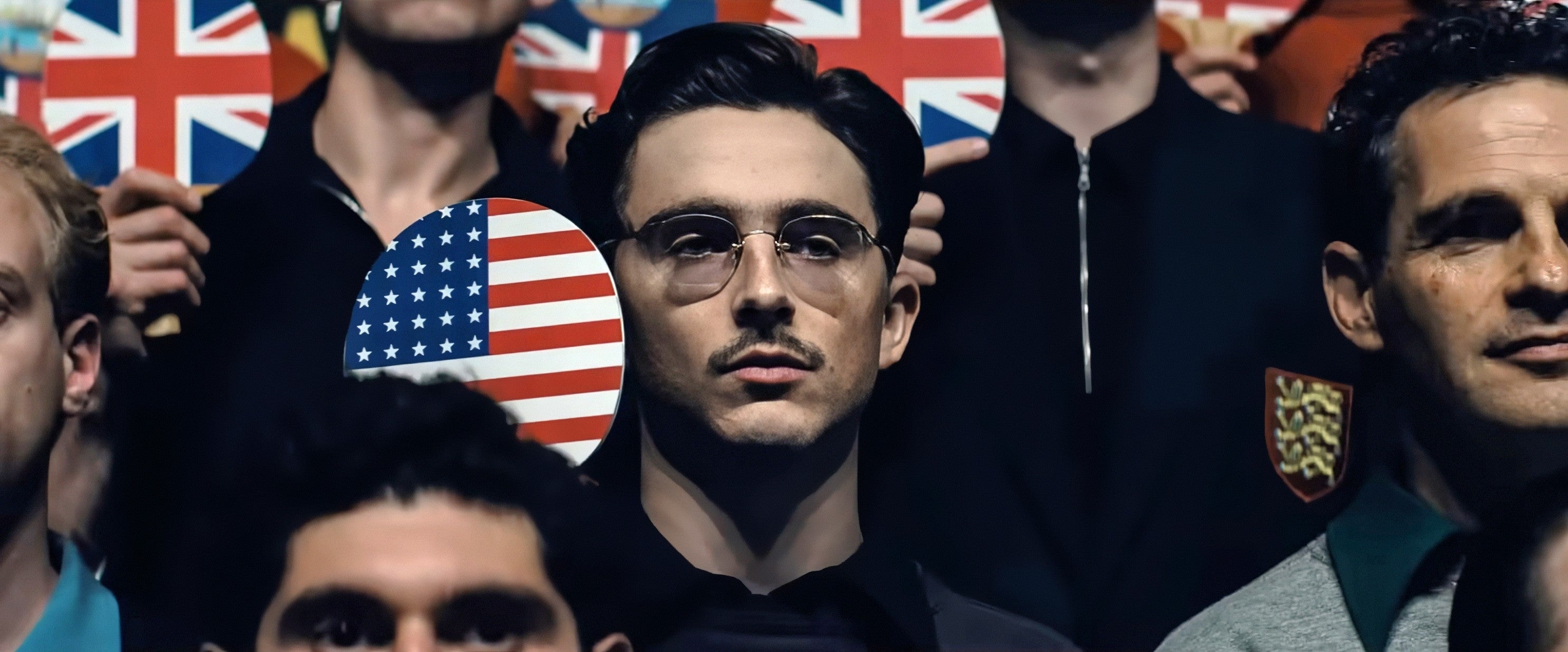 En mann med briller holder et lite amerikansk flagg blant en folkemengde, og skiller seg ut blant Union Jack-flaggene rundt