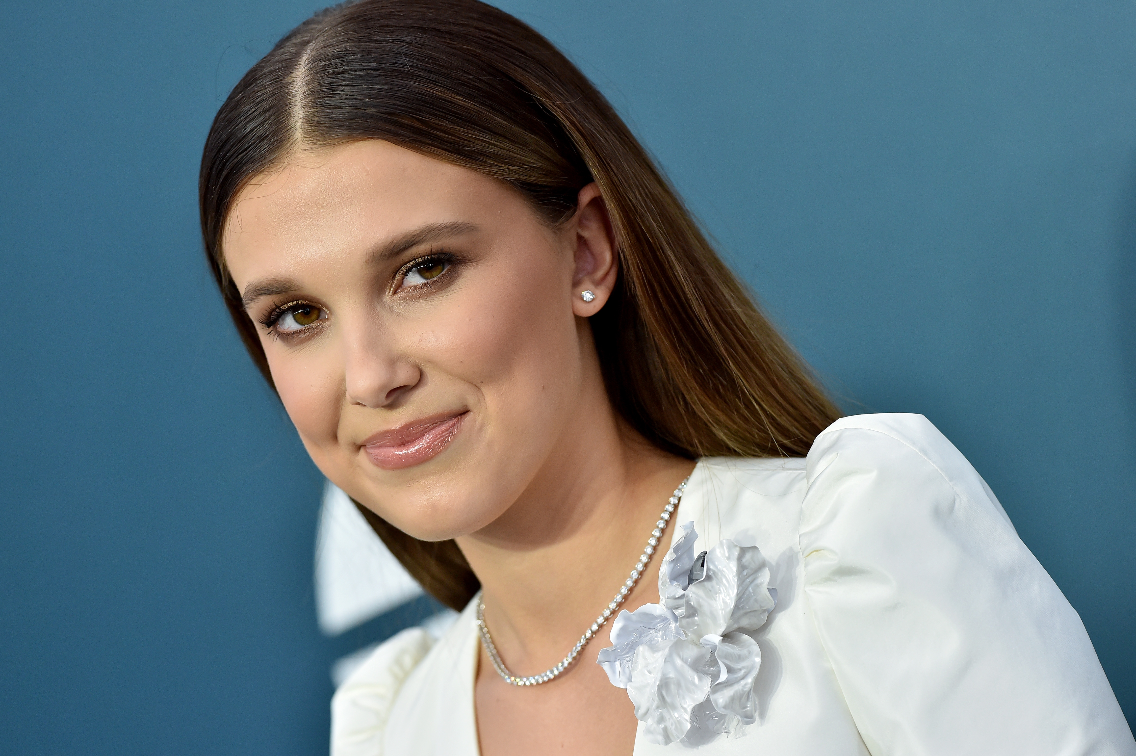 Millie Bobby Brown smiling, wearing a floral formal  with a pearl necklace, astatine  a nationalist   event