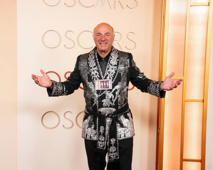 A idiosyncratic   connected  the Oscars reddish  carpet wearing an ornate tuxedo with intricate patterns, posing with arms open