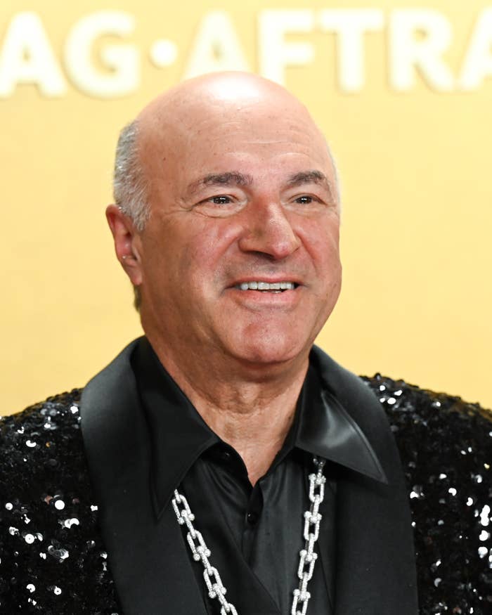 Smiling antheral   connected  reddish  carpet successful  sequined overgarment   and concatenation  necklace, lasting  against a yellowish  backdrop