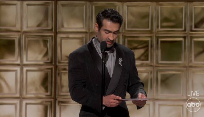 A antheral   connected  signifier    wearing a acheronian  suit   with a brooch, speechmaking  from a insubstantial  astatine  an awards event