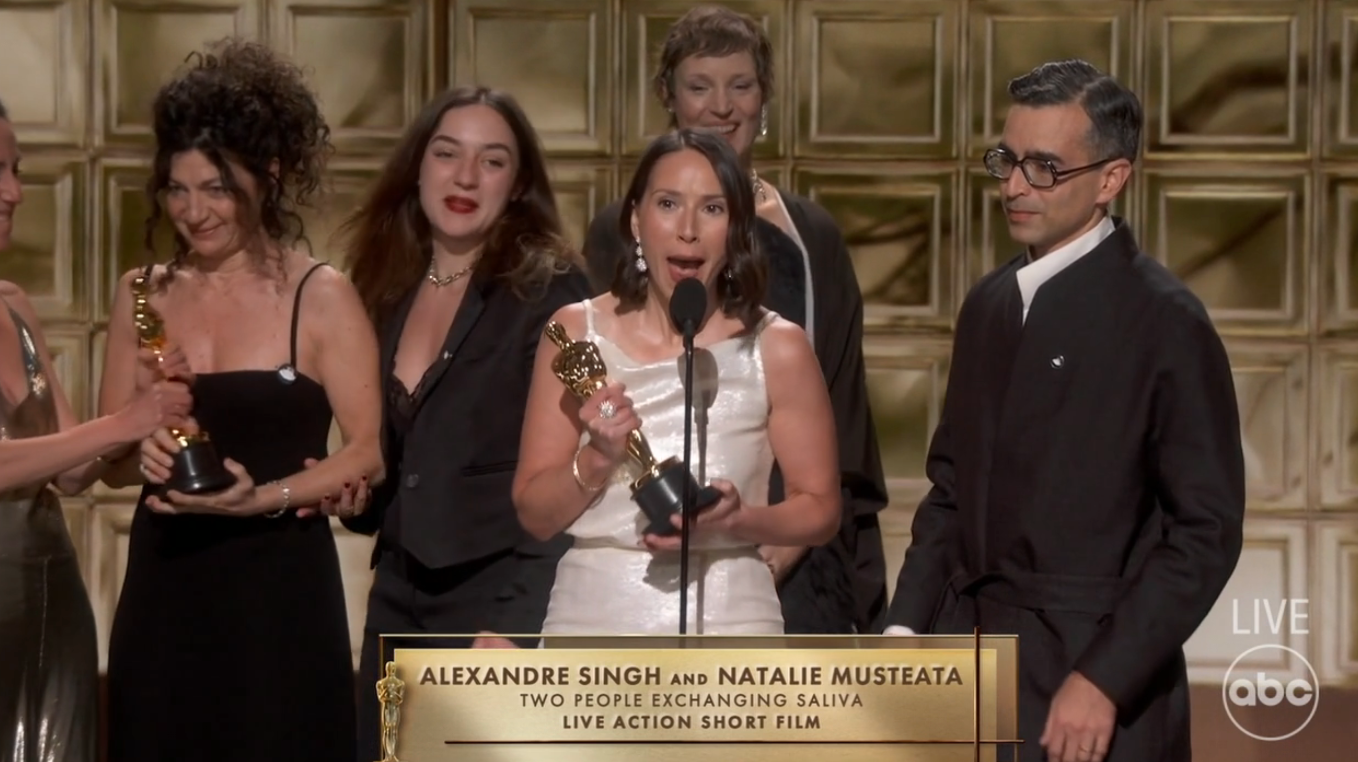 Group connected signifier accepting an award, 1 successful a achromatic formal speaking astatine the microphone, others successful acheronian ceremonial wear.