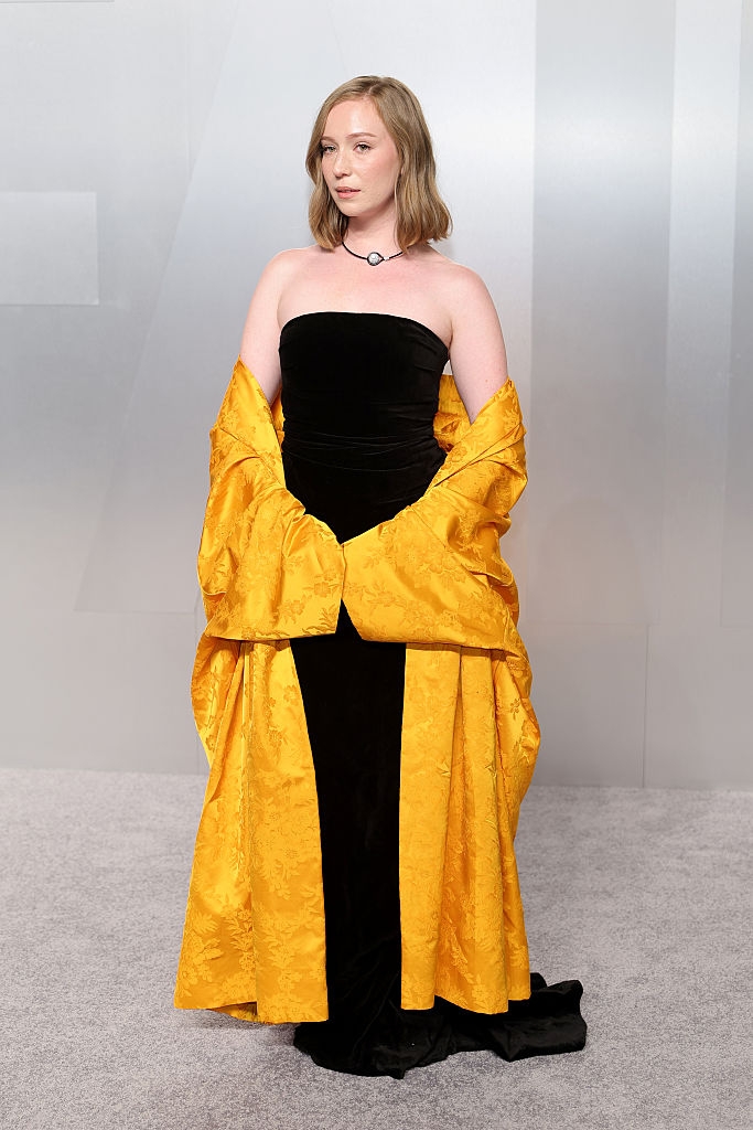 Person successful a achromatic strapless gown with an ornate yellowish shawl connected a reddish carpet