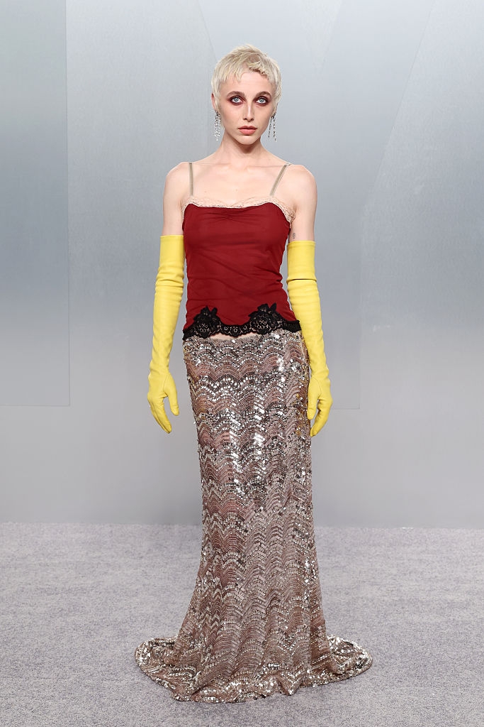 Person successful a reddish fitted top, yellowish gloves, and a long, sequined skirt with lace details, posing connected a neutral backdrop