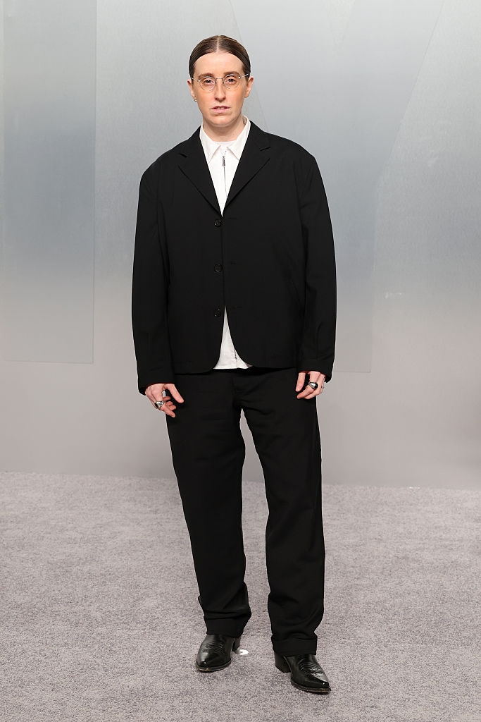 Person successful a sleek, tailored suit with circular glasses and rings connected fingers, posing for the camera