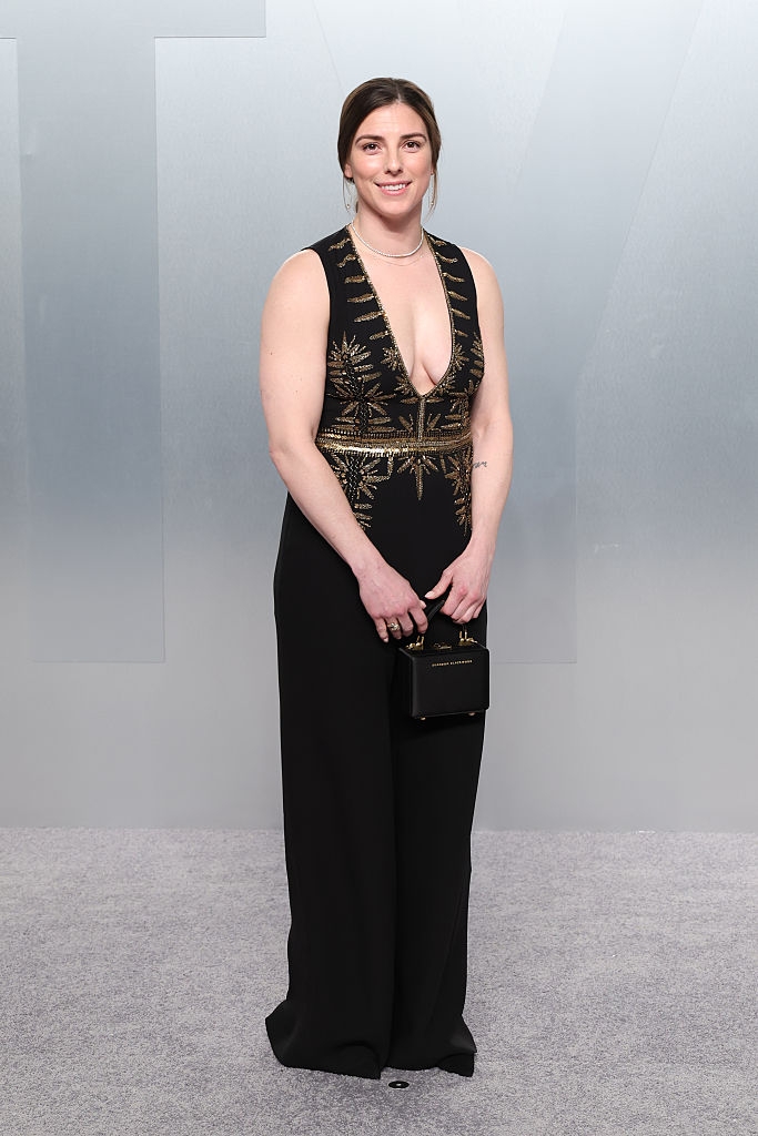 Person successful a sleeveless achromatic gown with golden patterns, holding a tiny achromatic clutch, posing connected a reddish carpet