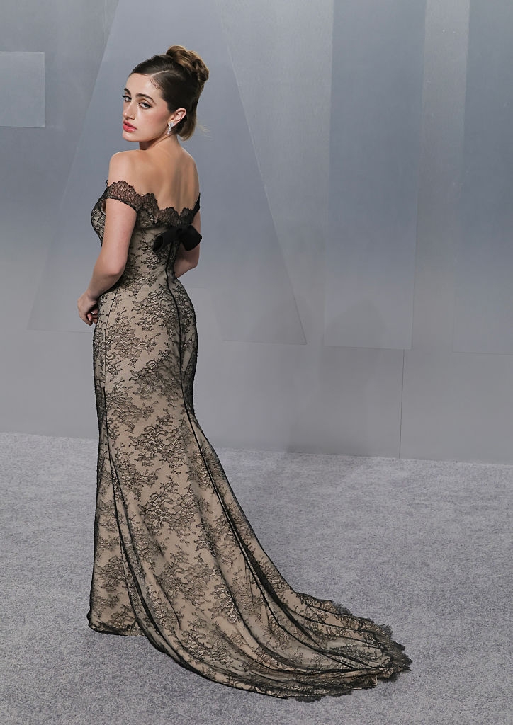 Person connected a carpet wearing an off-shoulder, lace gown with a train, looking backmost implicit their shoulder