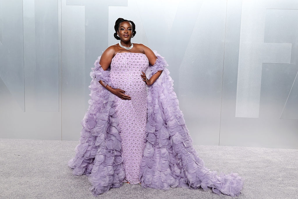 Person wearing a strapless patterned gown with a dramatic, flowing shawl, lasting connected a carpeted surface