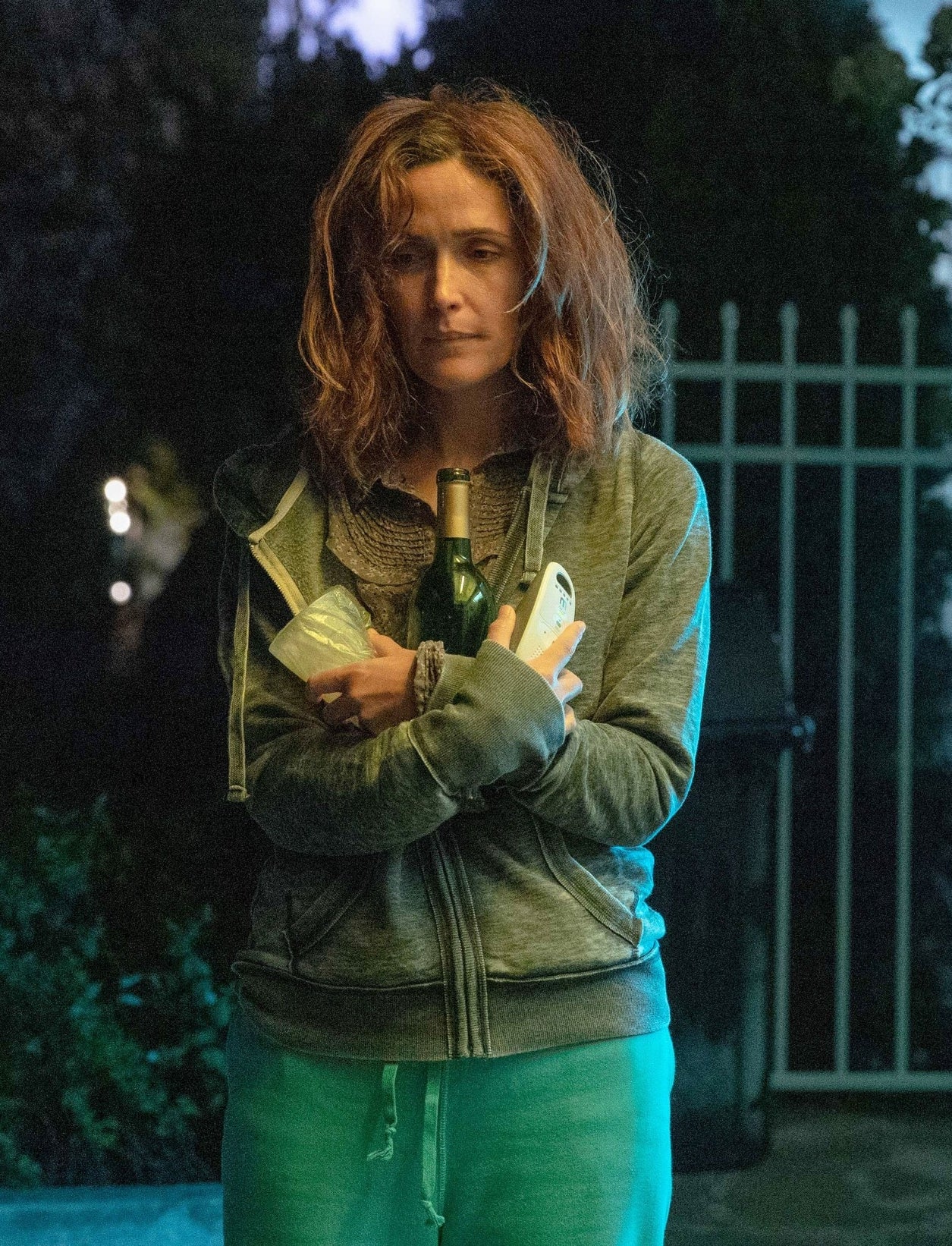 A idiosyncratic with disheveled hairsbreadth stands outdoors astatine night, wearing a casual outfit and holding objects, nether a blue-tinged light