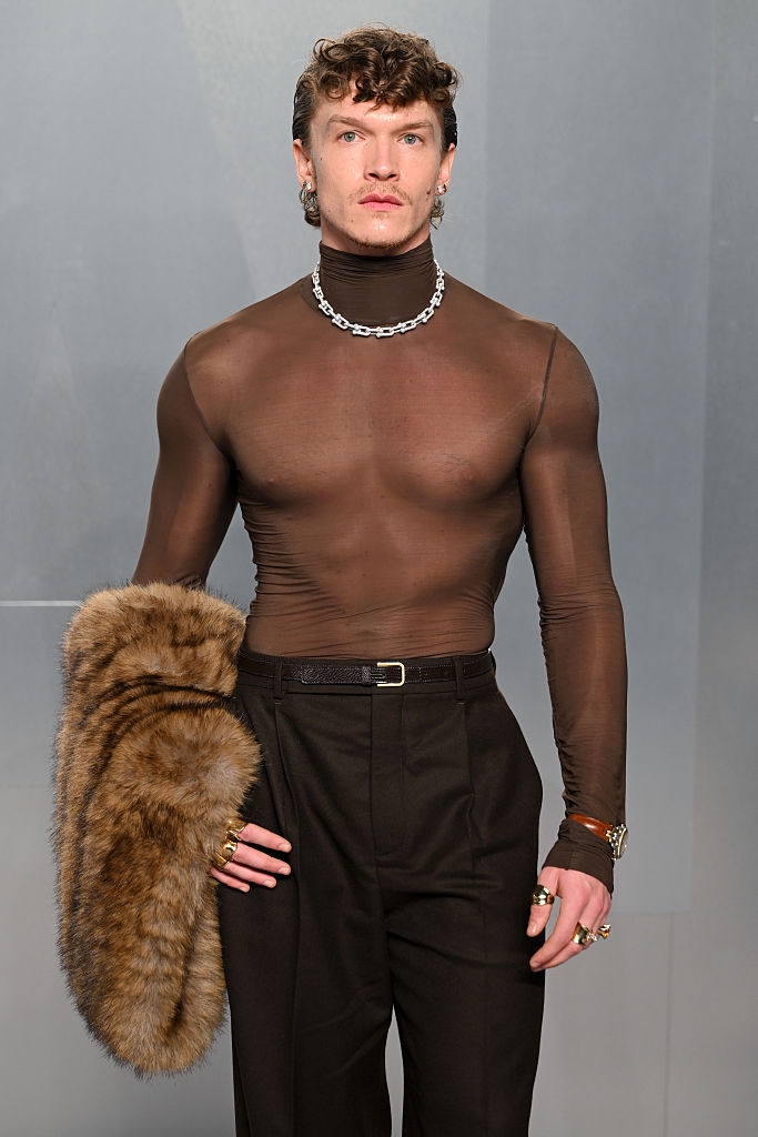 Person connected the runway successful a sheer apical and acheronian trousers, holding a fur accessory