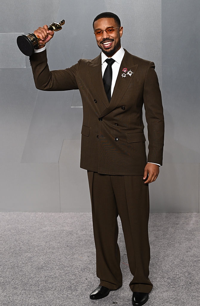 Man successful a tailored suit holds an grant trophy, smiling connected a stage, showcasing elegant style