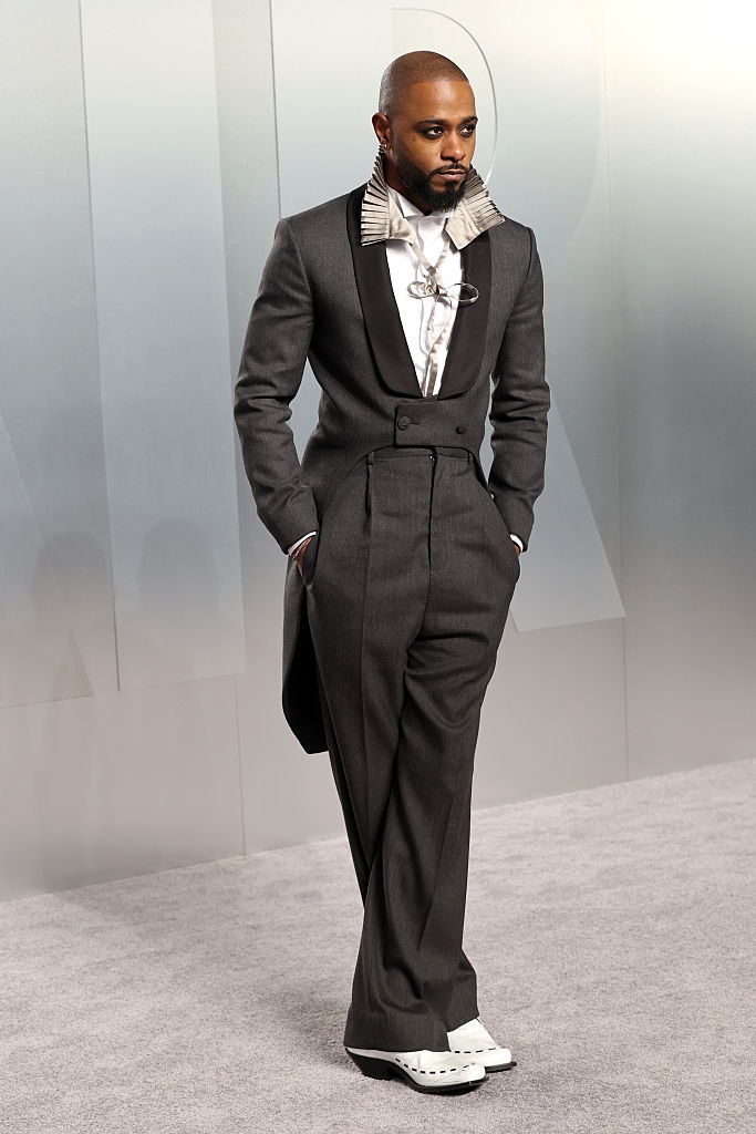 Person successful stylish tuxedo with wide lapels and unsocial collar item connected a grey carpet, hands successful pockets, astatine a personage event