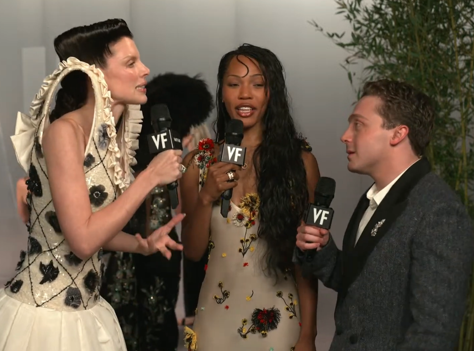 Three individuals holding microphones with "VF" logos, engaged successful conversation. They deterioration ceremonial attire, with unsocial designs and patterns