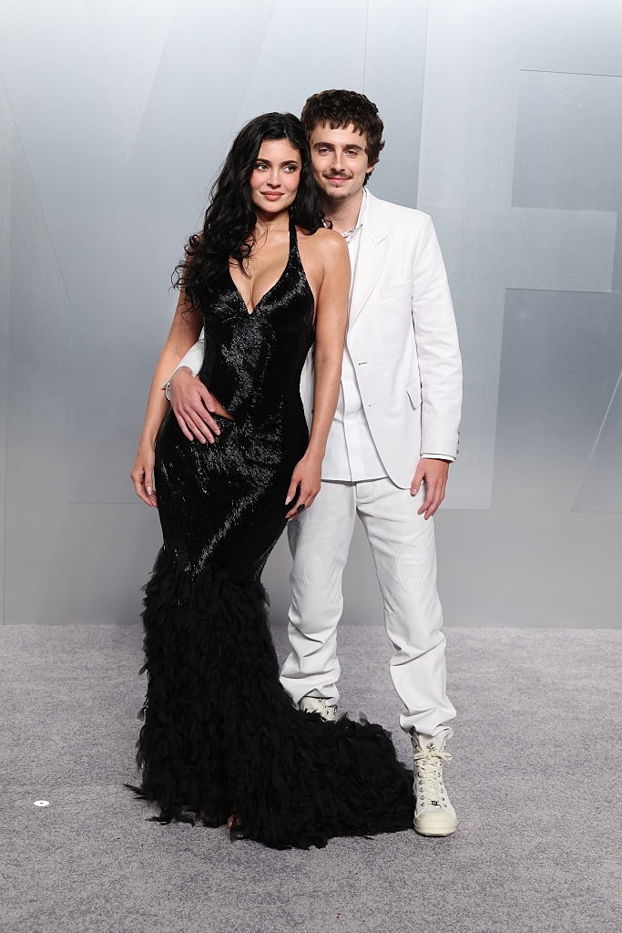 A antheral successful a achromatic suit and sneakers stands adjacent to a pistillate successful a black, sequined gown with a feathered bid connected a reddish carpet