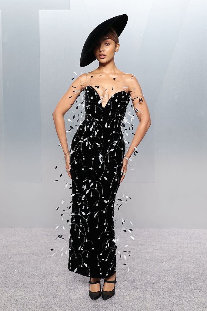Person successful an elegant strapless gown with intricate embellishments and a large, stylish hat, posing connected a ceremonial lawsuit carpet