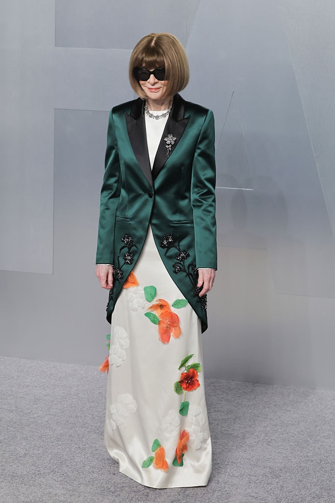 Person successful a satin blazer with floral embroidery implicit a agelong formal with vibrant floral patterns, wearing sunglasses