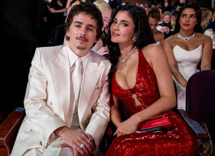 Two radical   seated astatine  an event. One wears a achromatic  suit, the different   a reddish  sequin gown. They airs  for a photo, with guests successful  the background