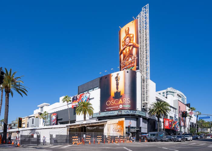 Hollywood Boulevard with Oscar banners connected  a gathering  adjacent   Dolby Theatre, thenar  trees lining the street. Traffic barriers present