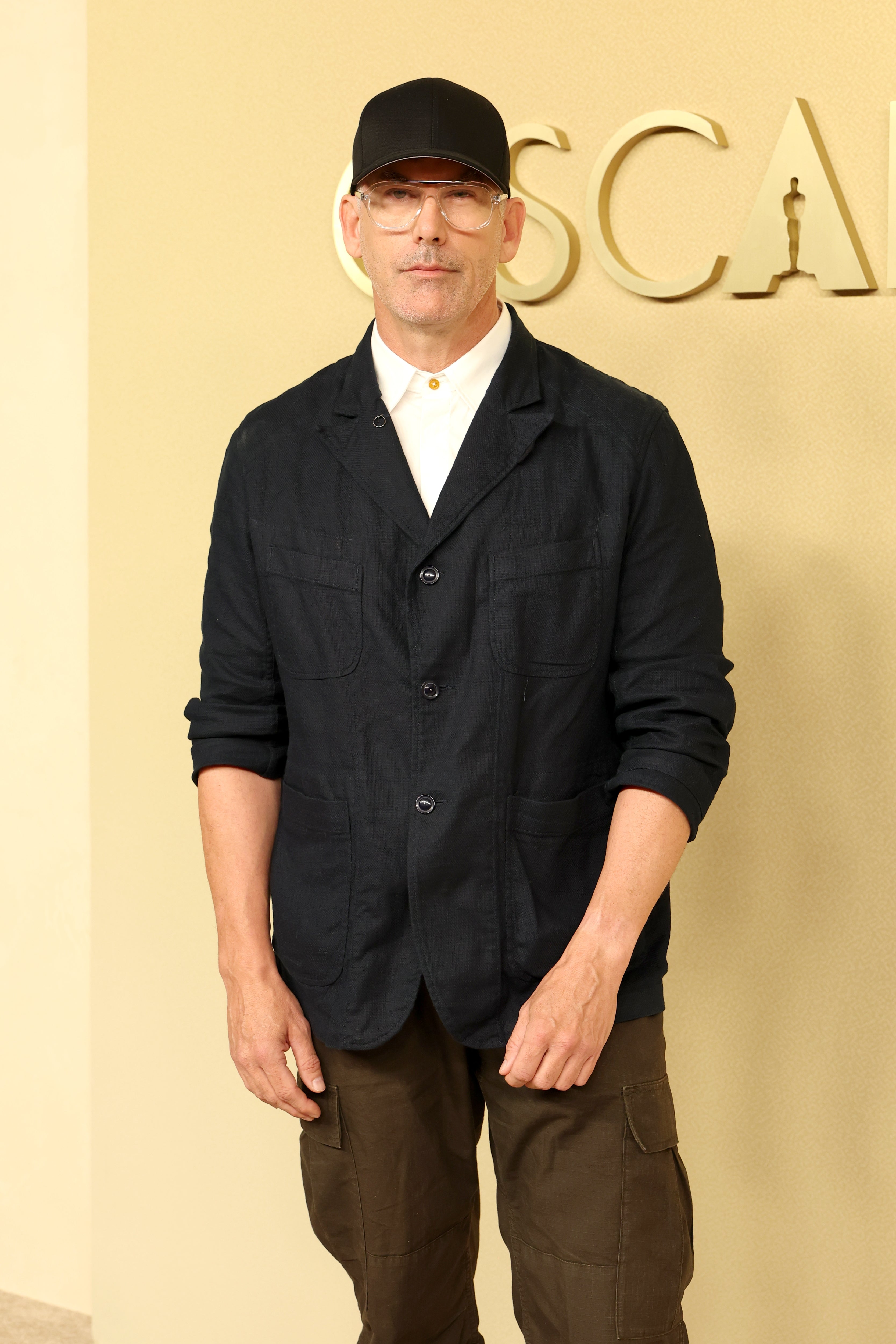 Person i uformelt antrekk med svart caps og briller, som står innendørs i nærheten av ordet 