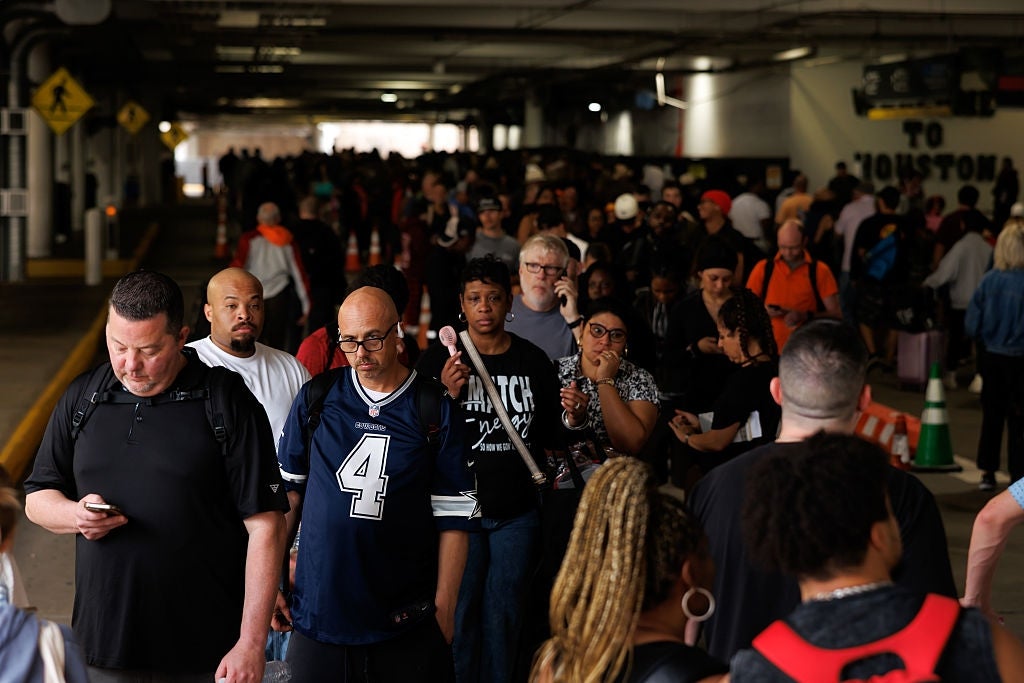 Folk venter i lang kø i innendørs omgivelser, muligens en flyplass eller transittområde