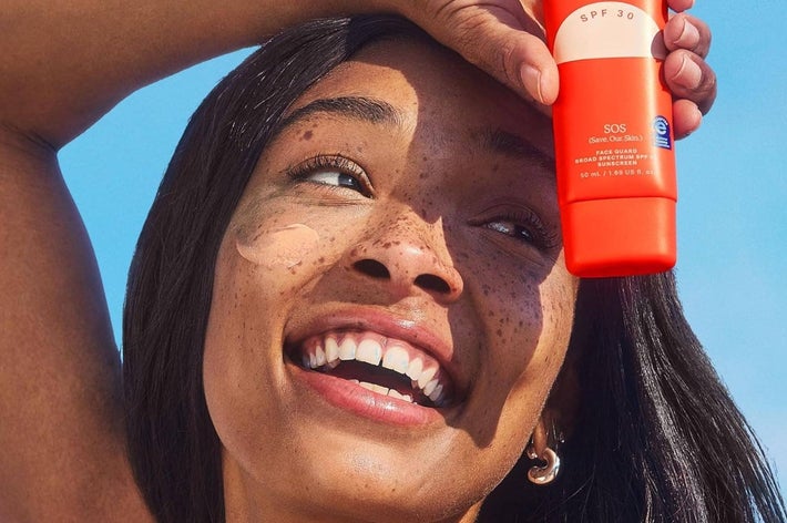 Woman smiling, applying sunscreen from an SPF 30 bottle. Image used in a shopping article