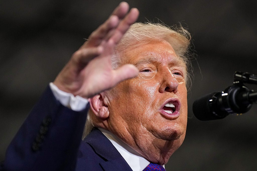 En person i dress snakker lidenskapelig ved en mikrofon og gestikulerer med en hånd løftet