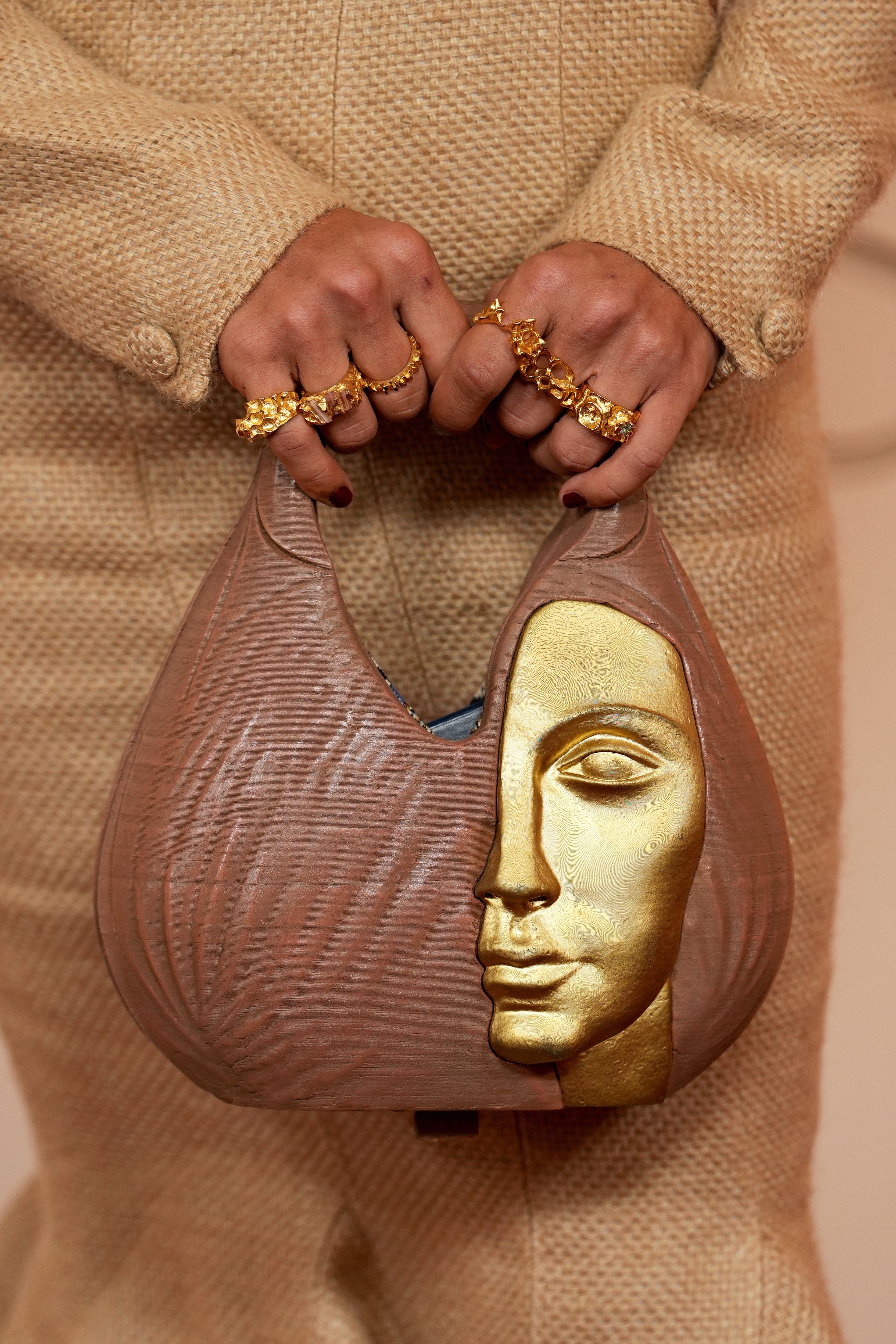 A idiosyncratic   holds a textured handbag featuring a sculpted golden  look   design, paired with golden  rings