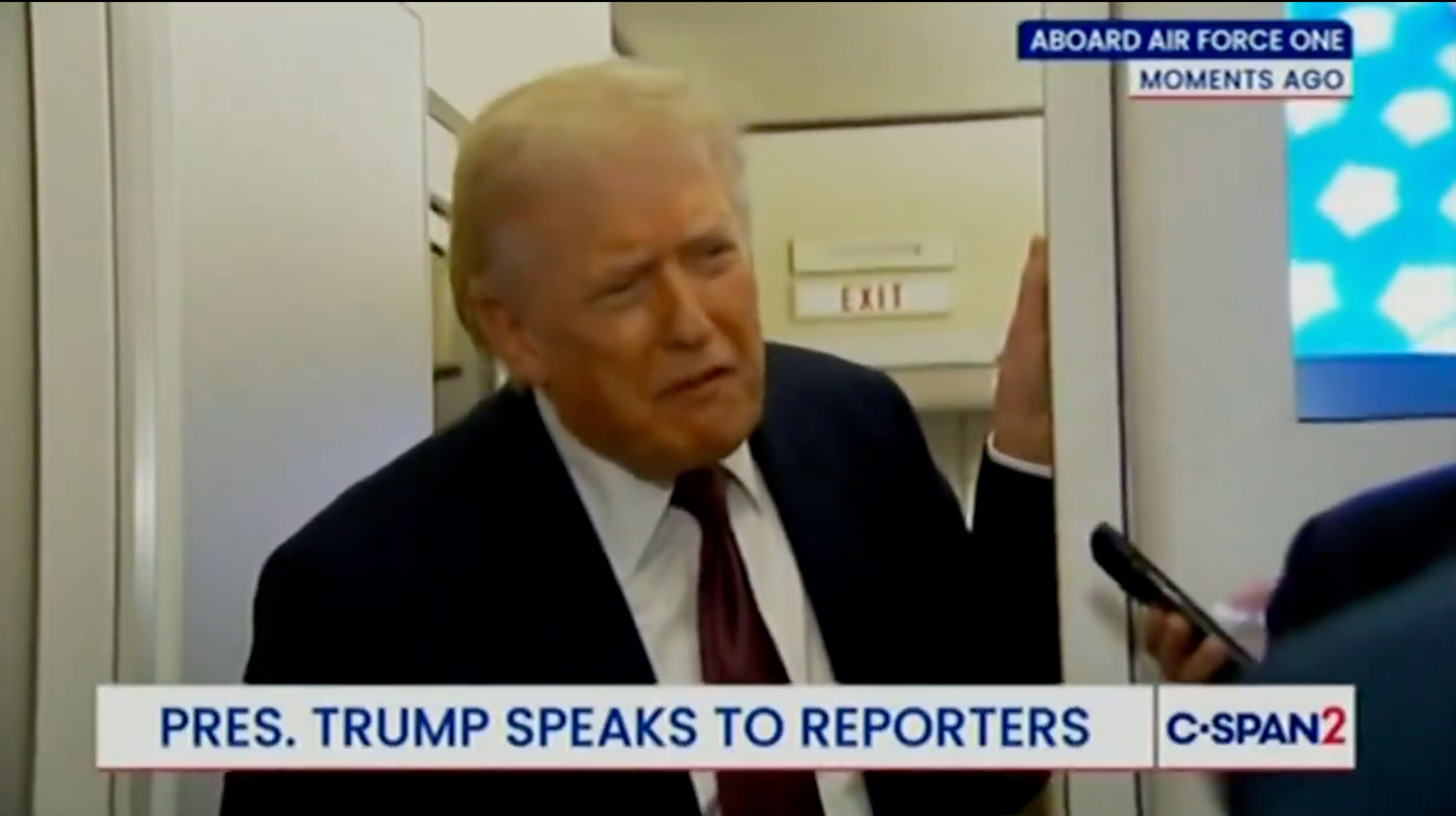 Mann i dress og slips snakker med journalister ombord på Air Force One