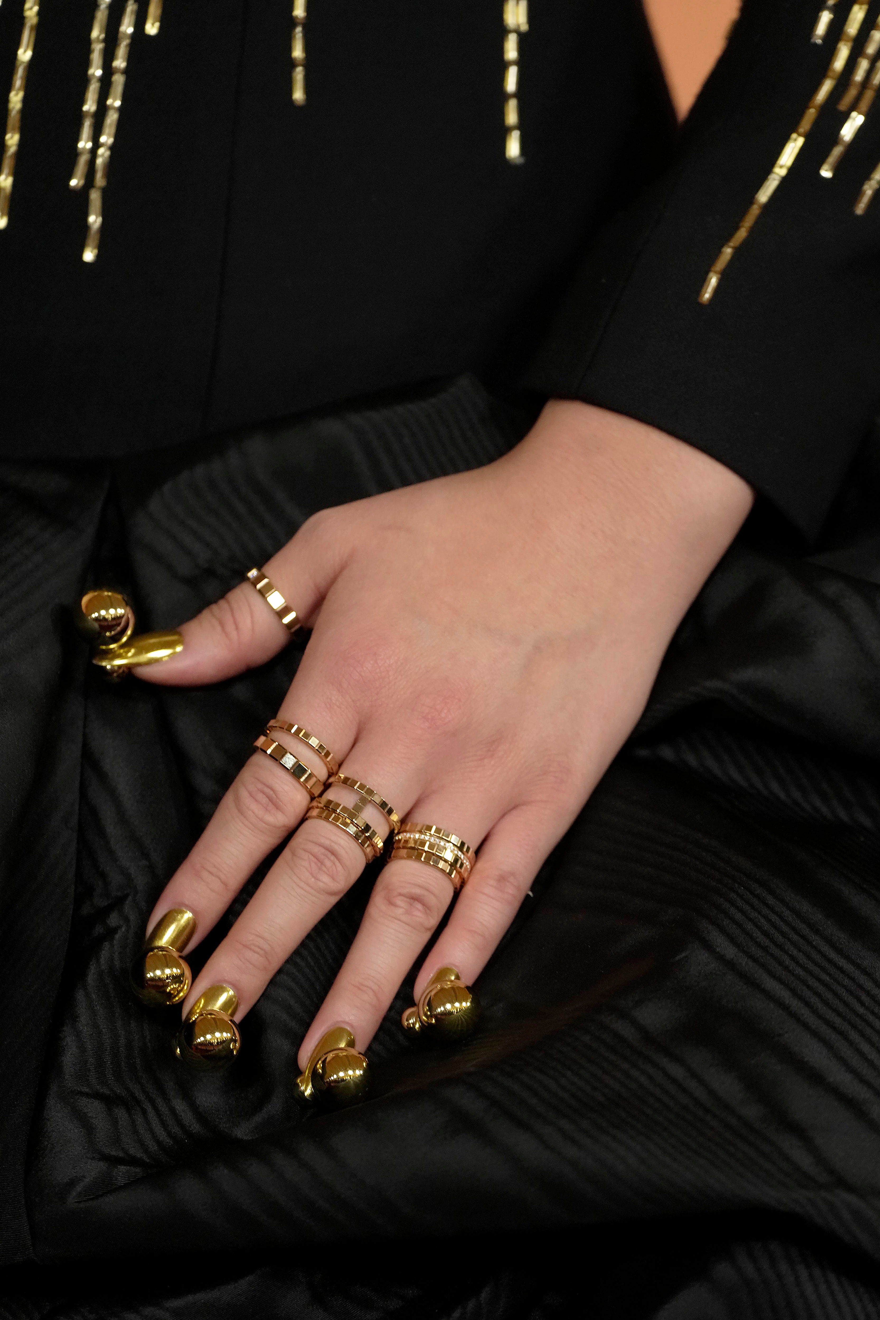 Close-up of a person's manus  adorned with aggregate  golden  rings and stylish golden  nail designs, resting connected  a achromatic  cloth  with golden  accents
