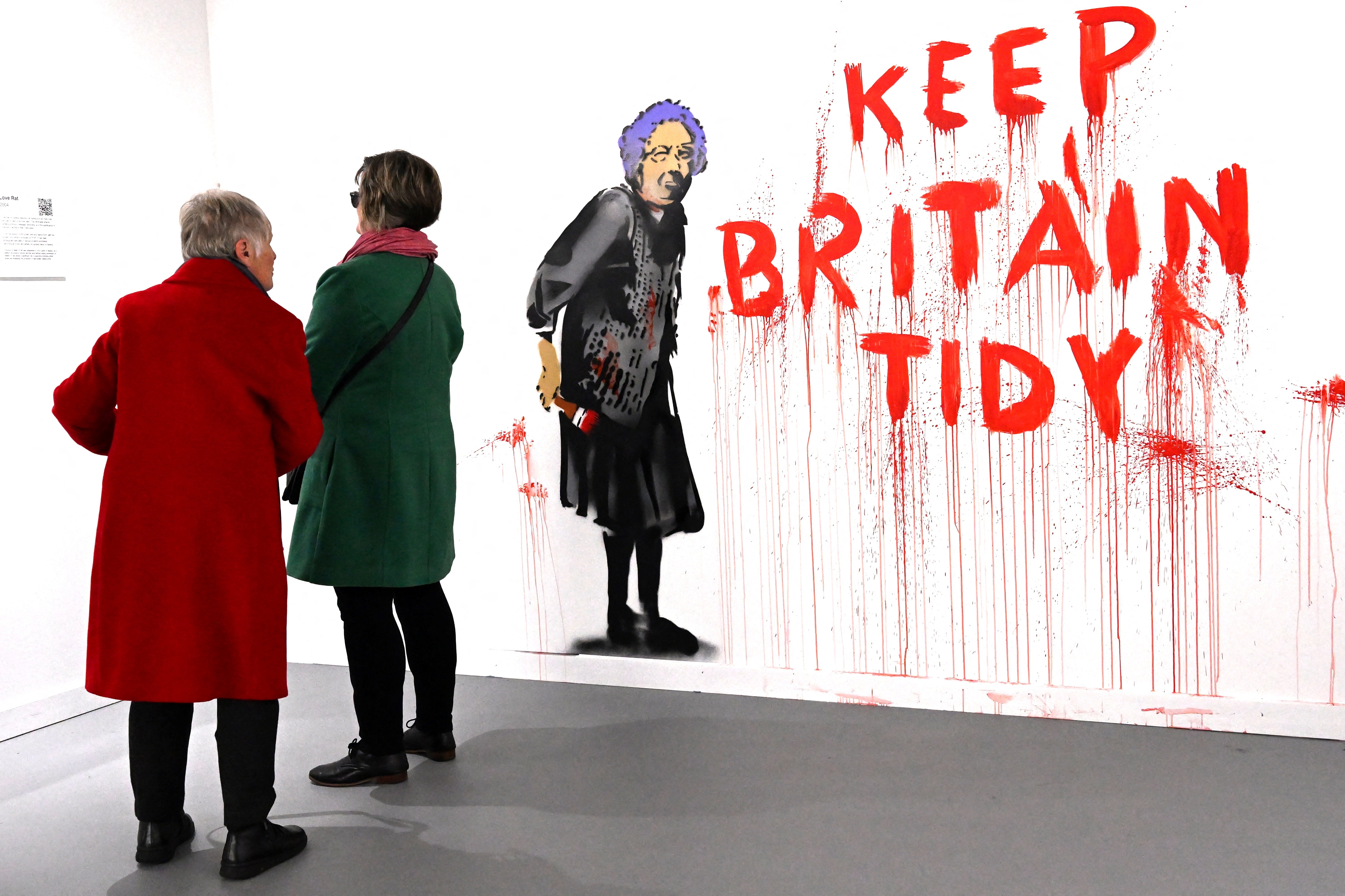To personer ser på graffiti av en kvinne med «Keep Britain Tyy»; i rød, dryppende maling på en gallerivegg