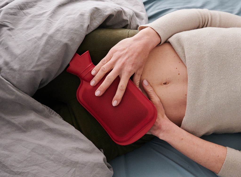 Person lying successful  bed, holding a blistery  h2o  vessel  connected  their abdomen, apt  for comfortableness  oregon  symptom  relief