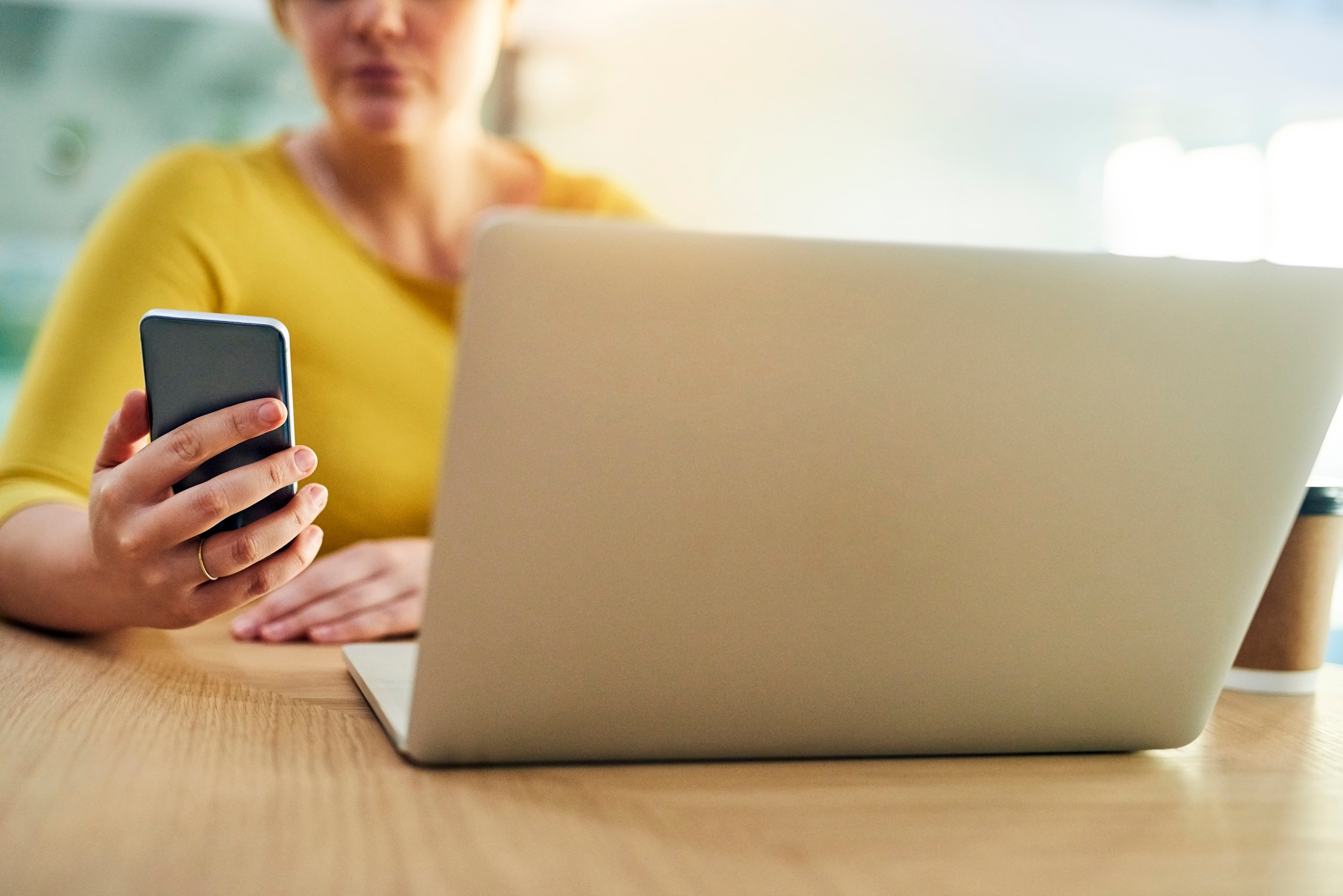 Person sitting astatine  a table  with a smartphone and a laptop, focusing connected  the phone