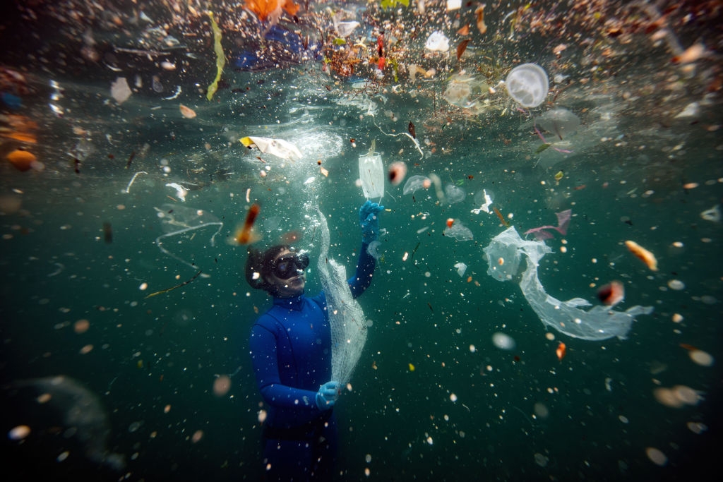 A diver successful  a wetsuit swims underwater surrounded by floating integrative  debris and trash, highlighting water  pollution