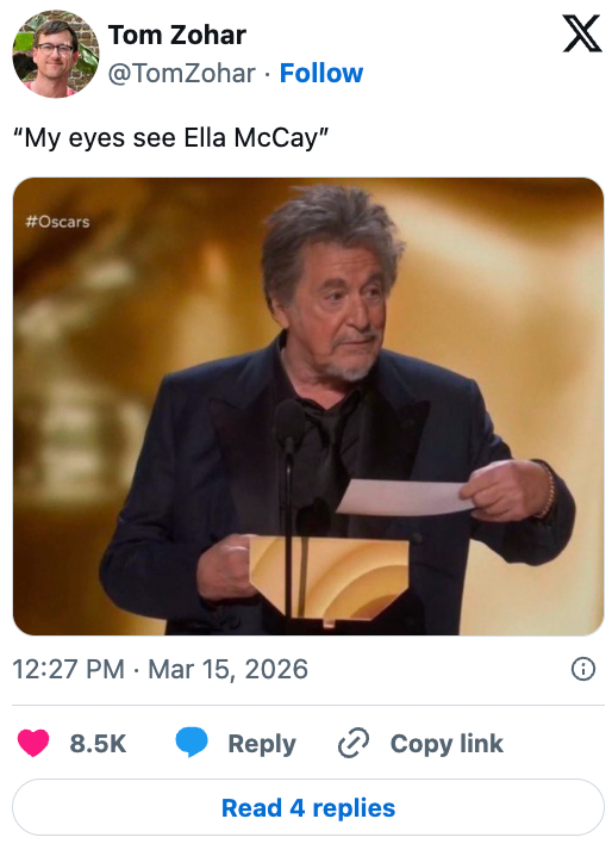 An older man in a suit holds an envelope on stage at an awards ceremony, speaking into a microphone