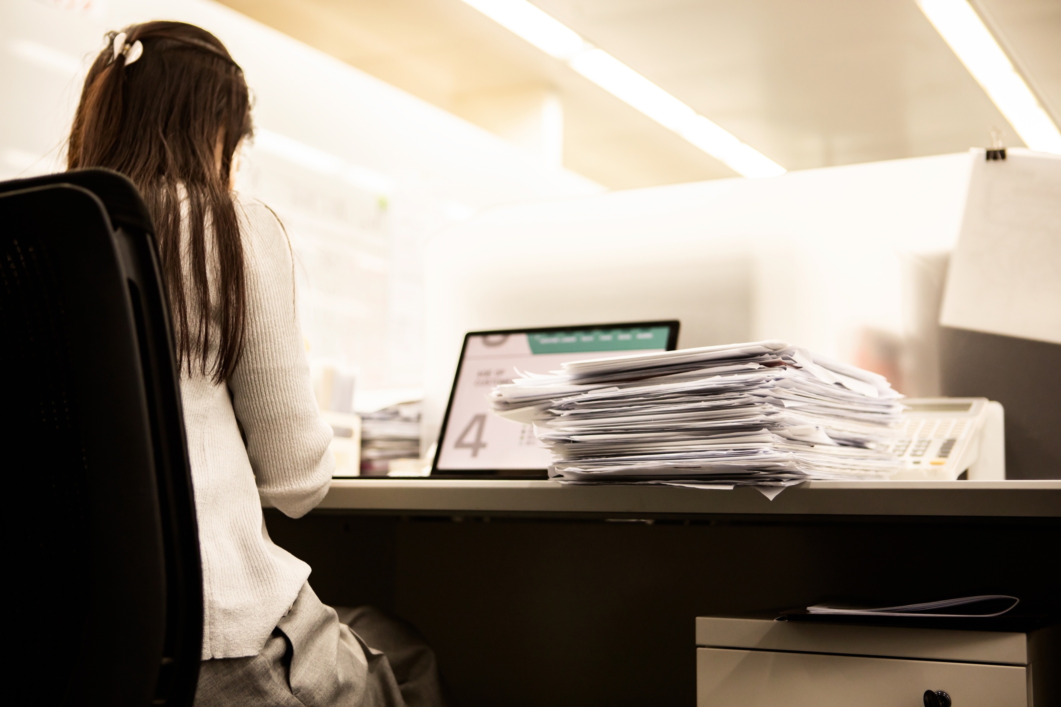 Person sitting astatine  table  with ample  stack of papers, moving   connected  a laptop. Office situation  with modern   furniture