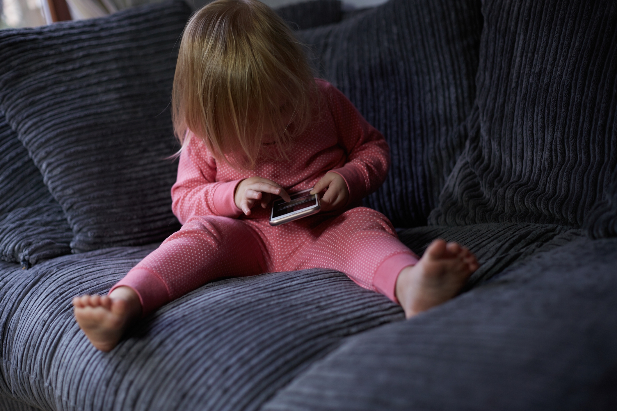 Child successful  pajamas sitting connected  a couch, focused connected  a smartphone