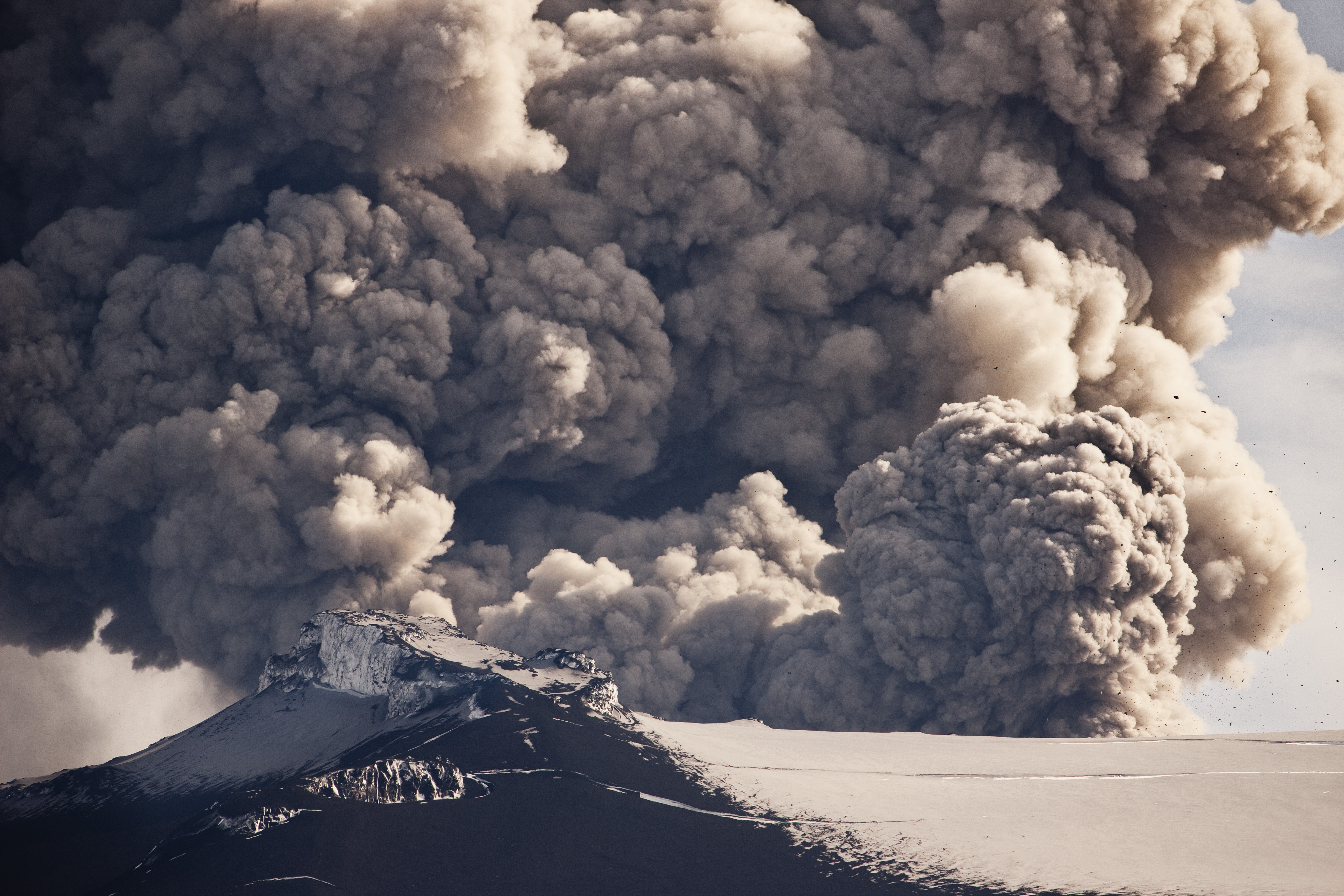 Volcanic eruption with monolithic  fume  and ash clouds rising supra  a snow-covered upland  peak