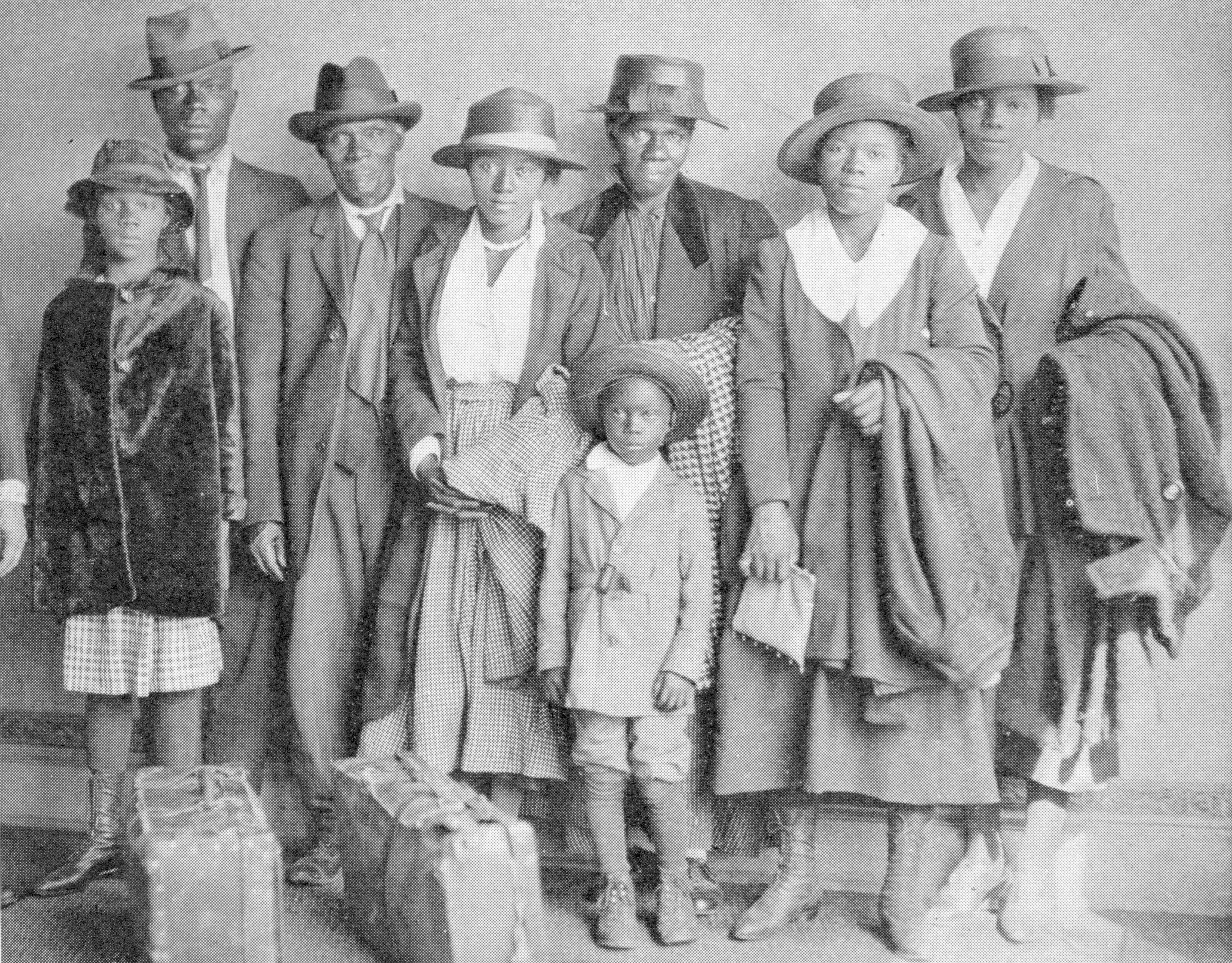 Historical photograph  of a Black household  successful  the aboriginal  20th century, wearing ceremonial  hats and coats, lasting  with luggage arsenic  if posed for question   oregon  migration