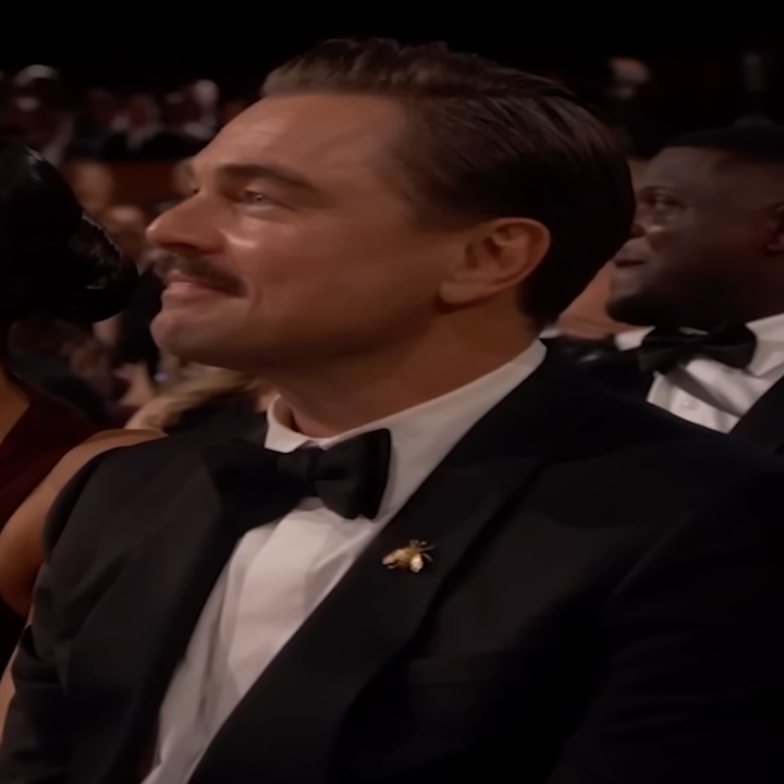 Um homem sentado de smoking com outros participantes formalmente vestidos em uma premiação