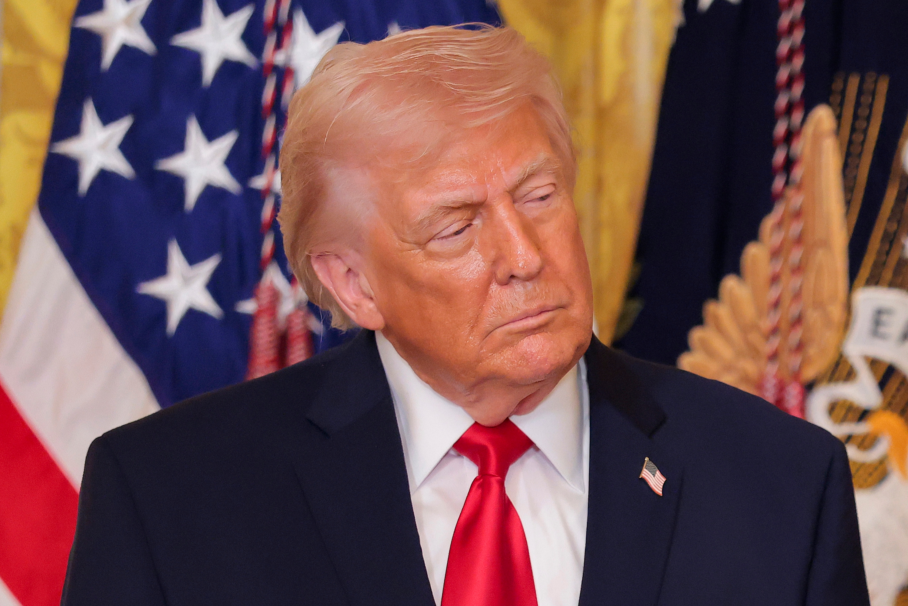 A idiosyncratic   successful  a suit   and reddish  necktie  stands successful  beforehand   of American flags, looking to the broadside  during an event