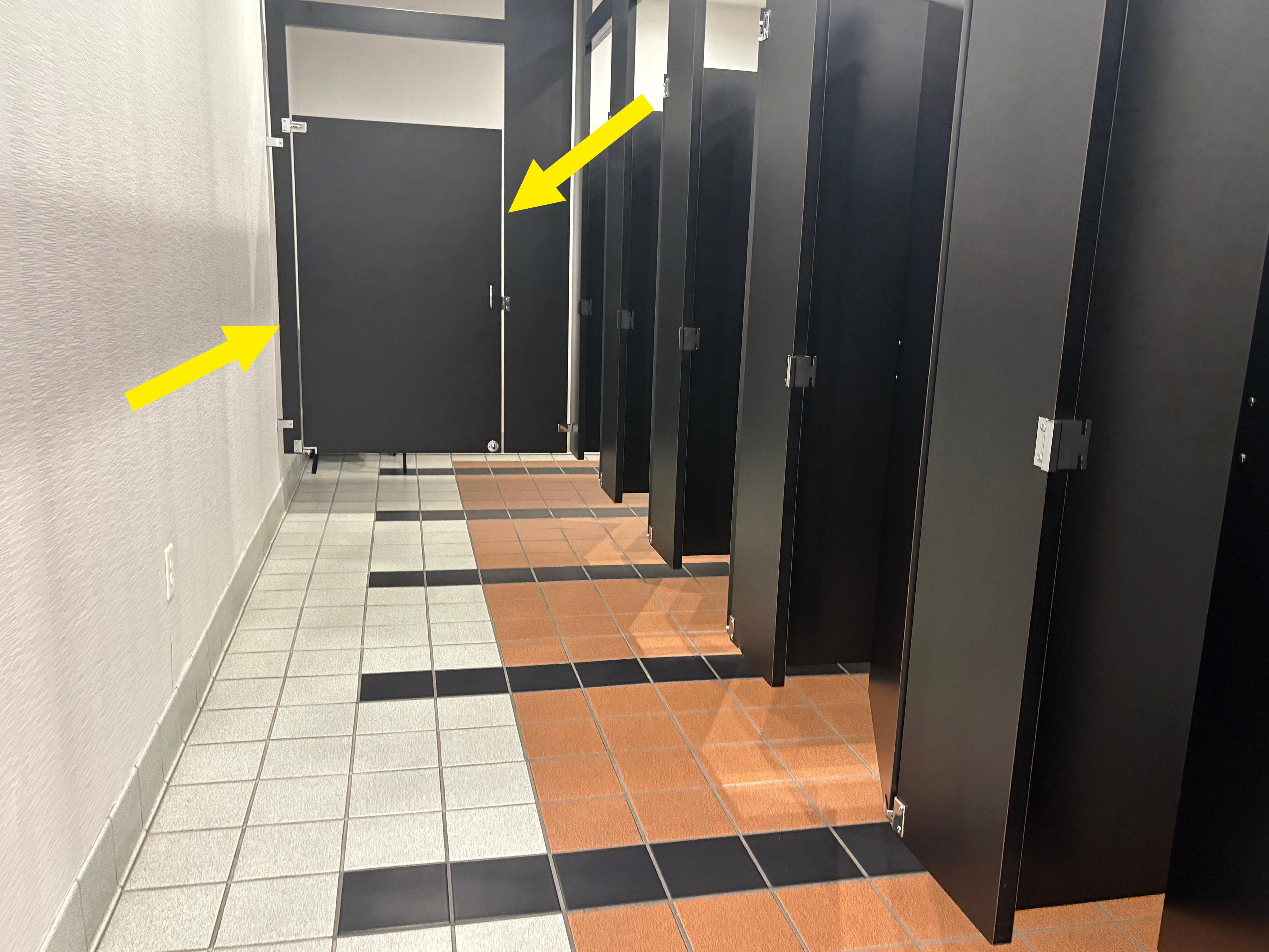 View of a nationalist   restroom with a enactment      of closed achromatic  stall doors and a premix  of tile patterns connected  the floor