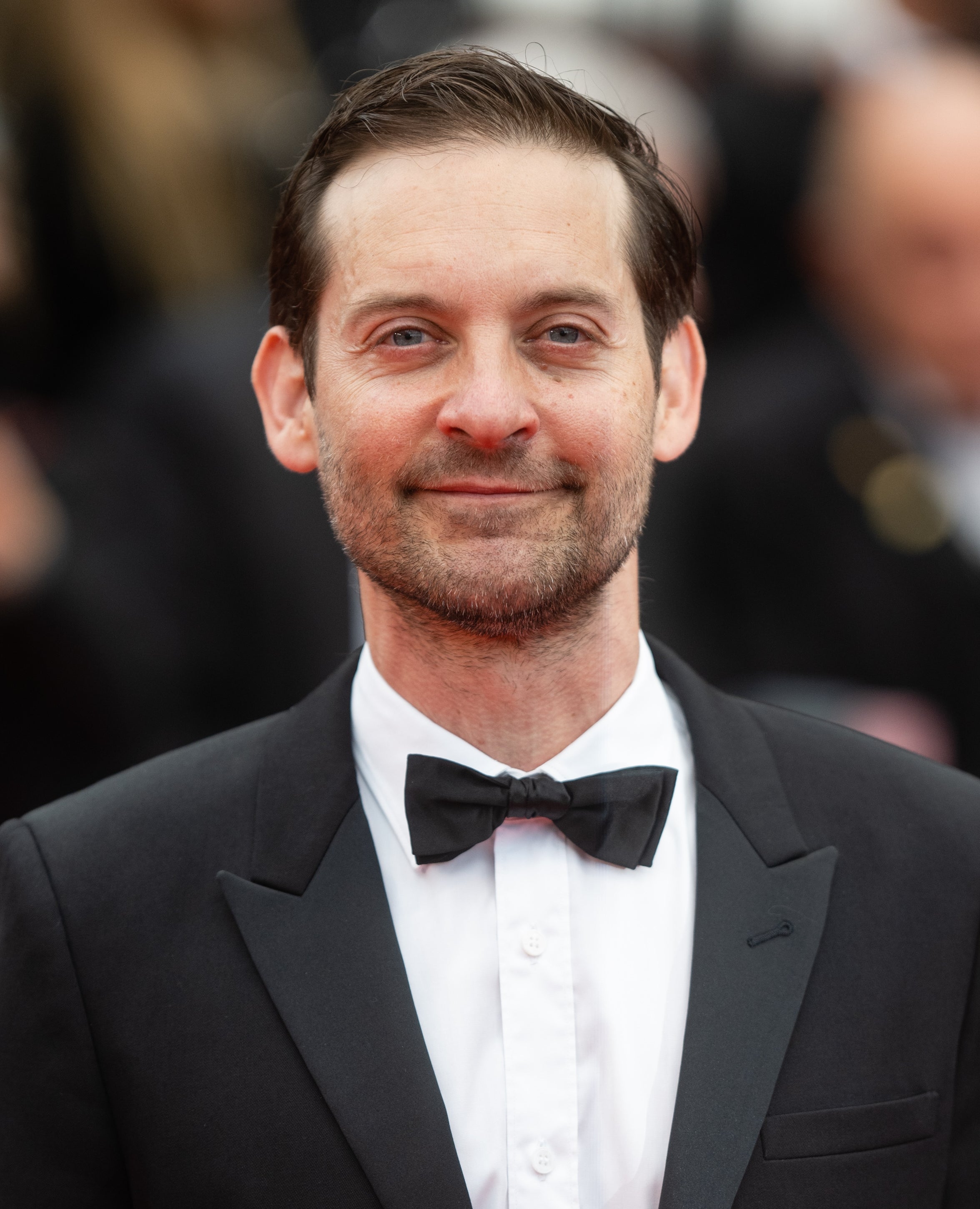 Tobey Maguire successful  a classical  tuxedo and bow necktie  connected  the reddish  carpet, smiling astatine  the camera