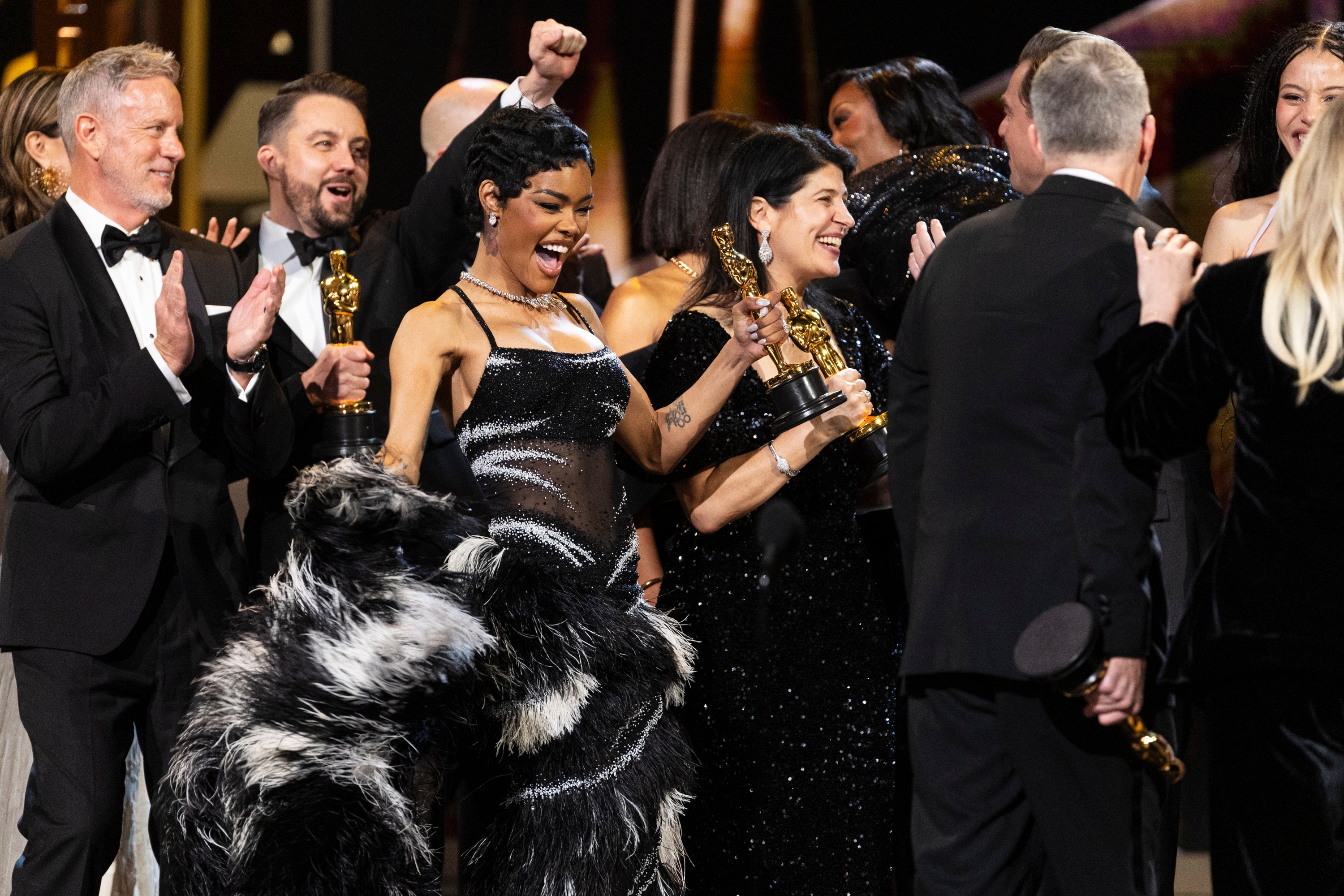 Group of celebrities celebrating onstage astatine  an awards ceremony, holding golden  statuettes. A pistillate   successful  a melodramatic  feathered gown is prominent