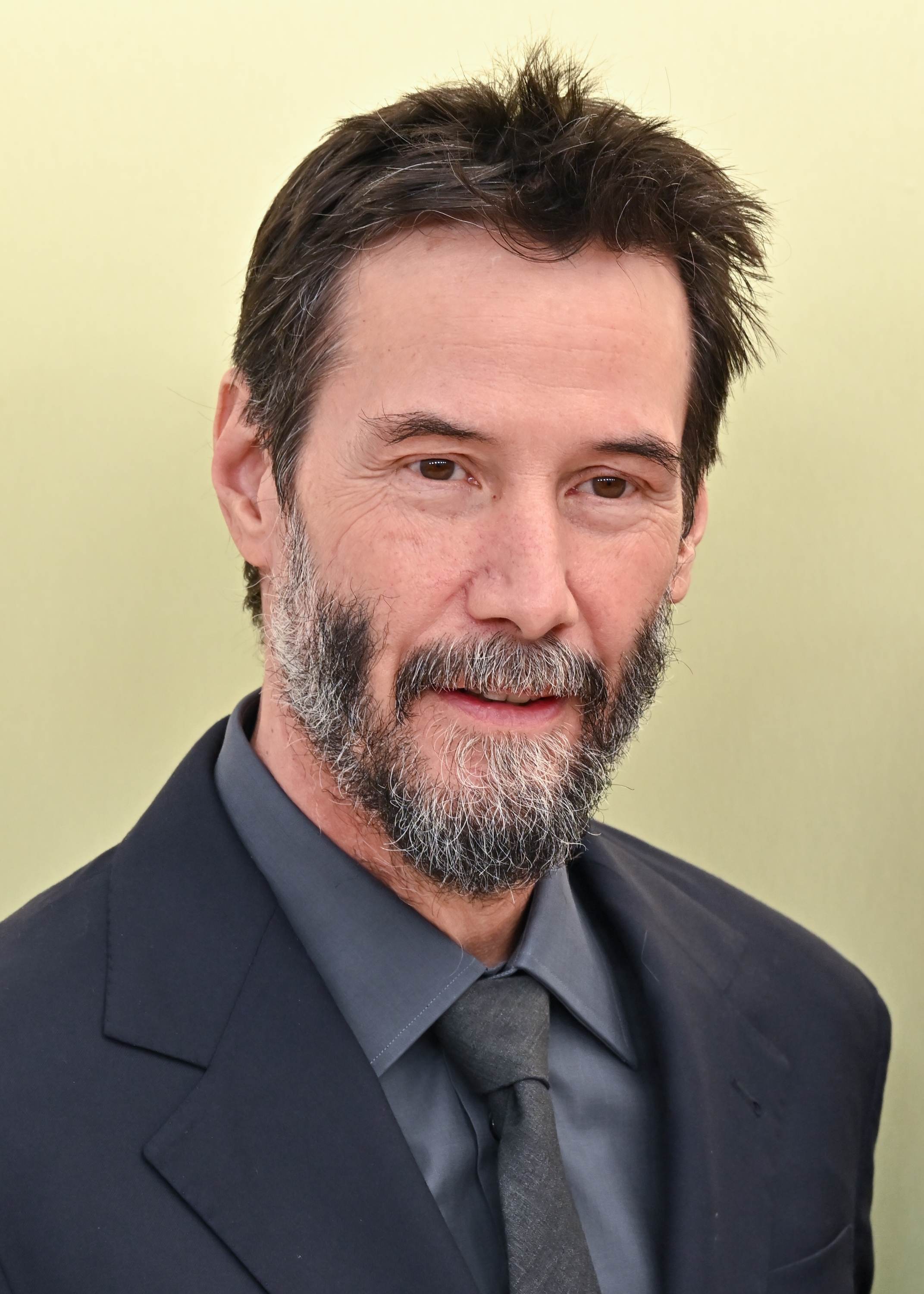 Keanu Reeves successful  a suit   with a beard and abbreviated  hair, poses connected  a reddish  carpet, looking straight  astatine  the camera