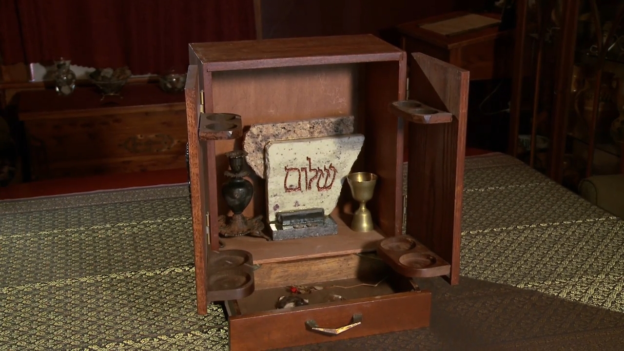 Wooden container unfastened to uncover ritual objects including chromatic tablet with Hebrew text, goblet, and containers, acceptable connected a cloth-covered table