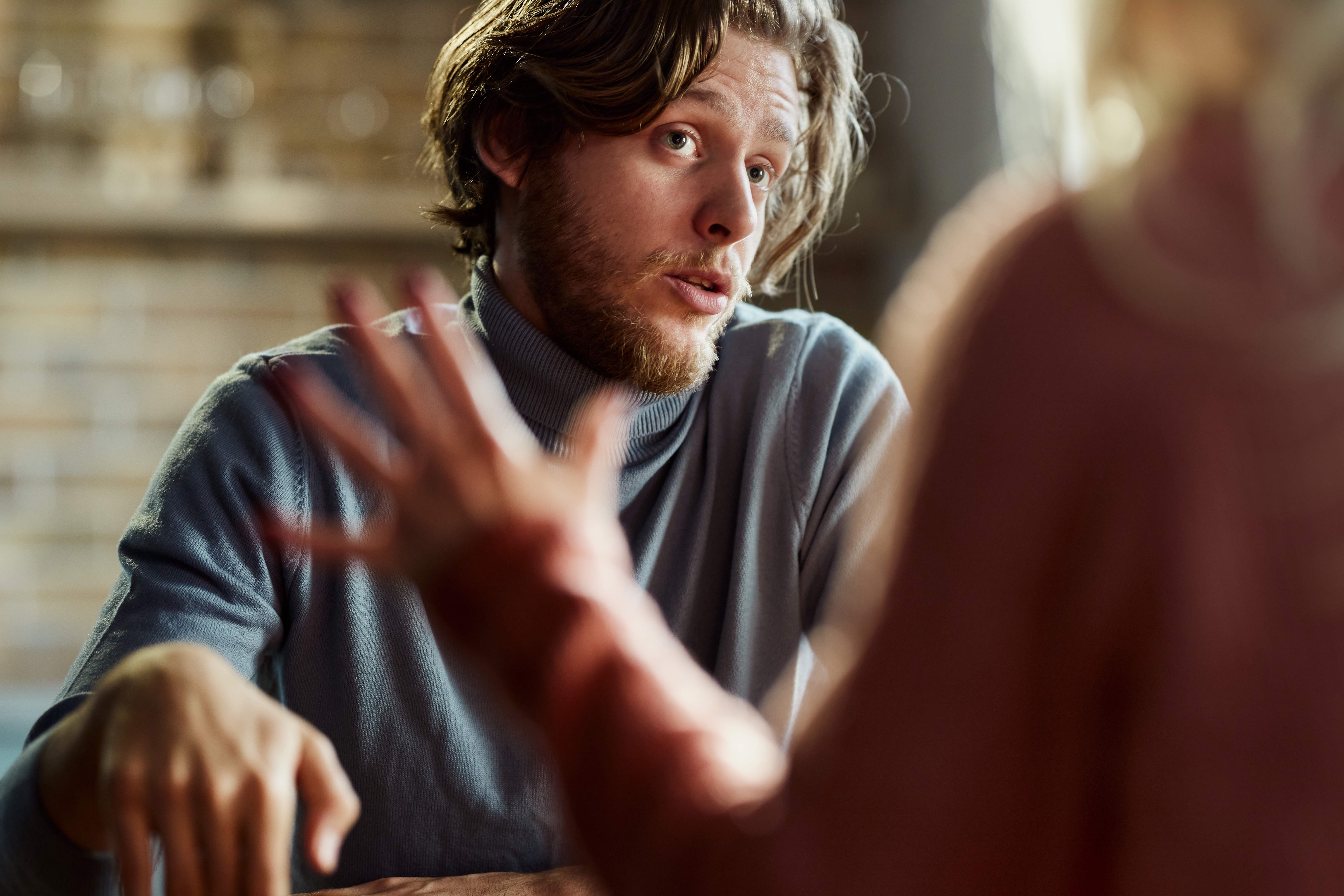 A man attentively listens to a woman gesturing during a conversation, indicating an intimate or serious discussion
